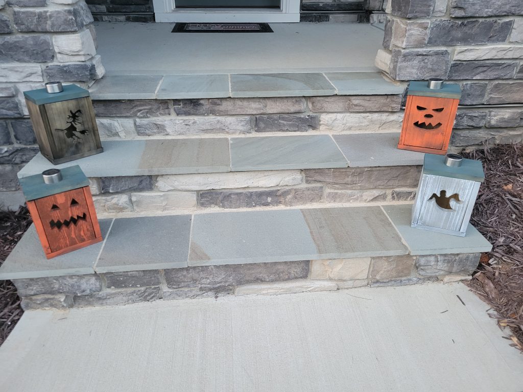 Finished Halloween lantern boxes on porch steps in daylight with solar light stems installed
