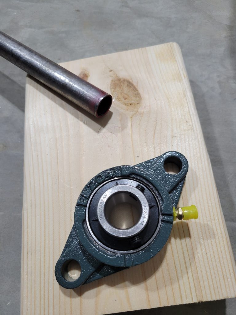 Bearing block and metal rod staged for the custom rock tumbler roller assembly.