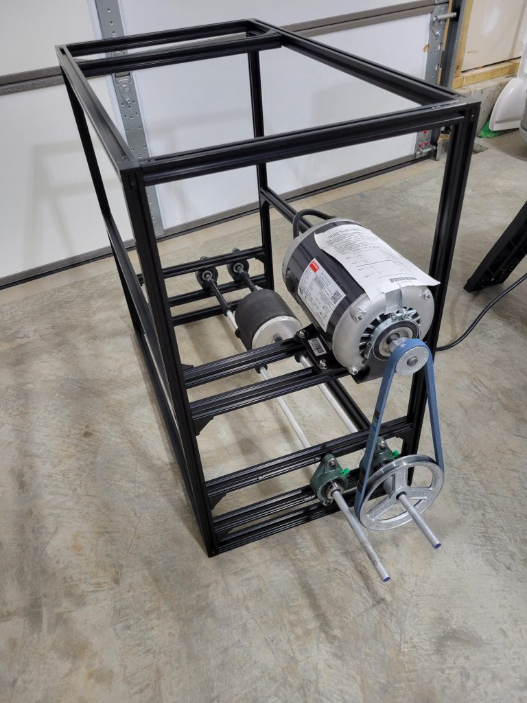 2020 aluminum extrusion frame with Dayton motor, rollers, and pulley hardware during assembly.