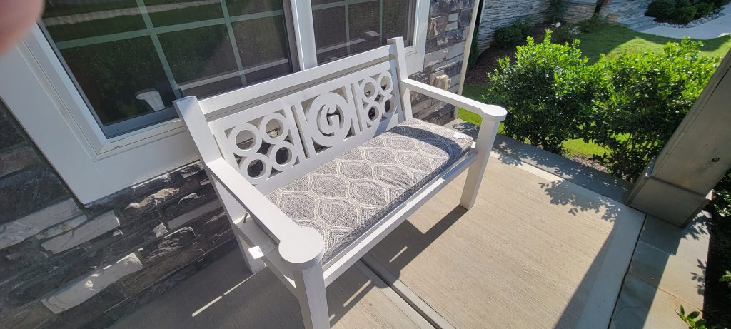 White front porch bench with patterned cushion being checked under the window