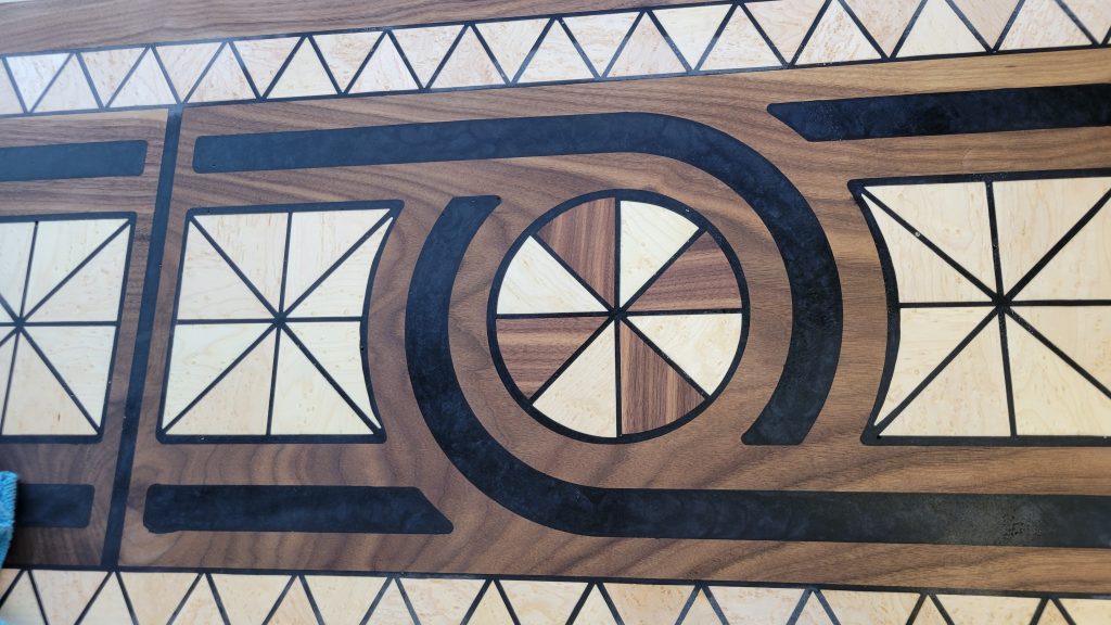Flattened walnut table top showing birdseye maple inlays and black epoxy lines after resin work