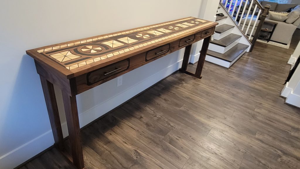 Finished walnut entry table viewed from the side with patterned inlay top and drawer front visible