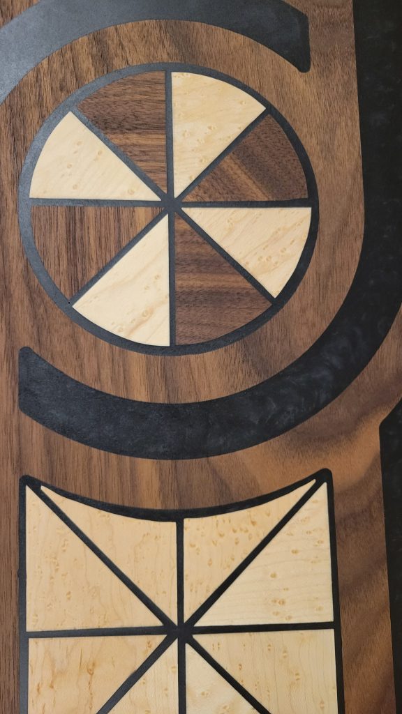 Close detail of circular walnut and birdseye maple inlay pieces separated by black epoxy