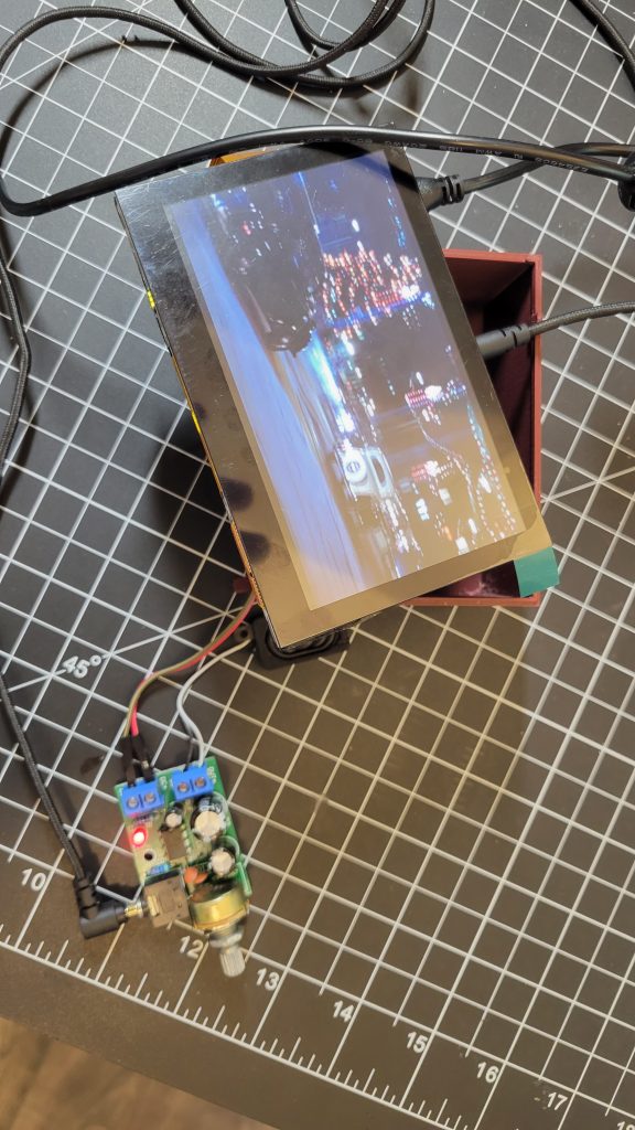 LCD, printed case, wiring, and potentiometer control hardware laid out on a cutting mat