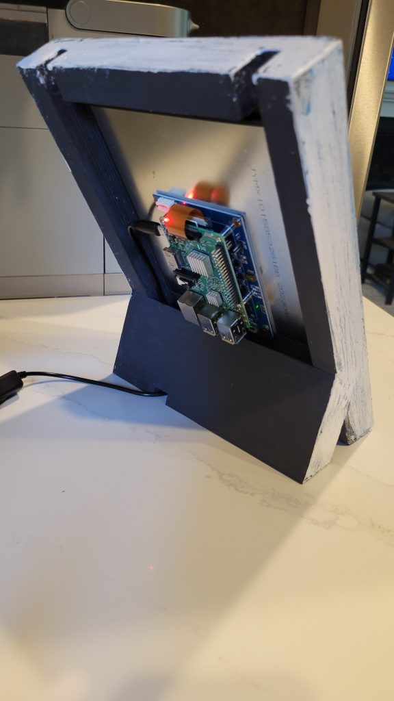 Back of the handmade frame showing the LCD, small computer board, wiring, and power hardware