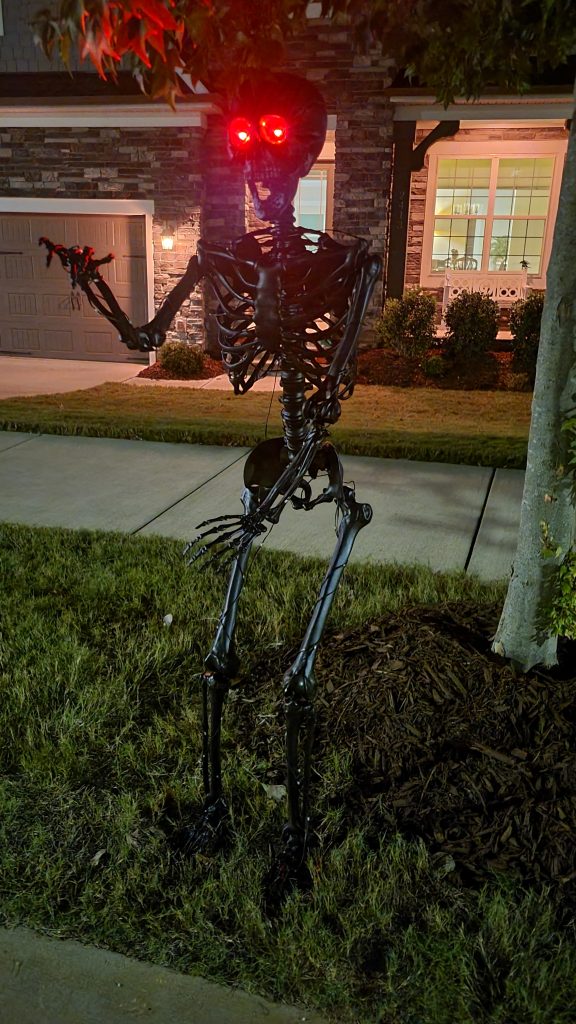 Matte black Halloween skeleton in the front yard with red eyes visible before the warm light-strip reveal
