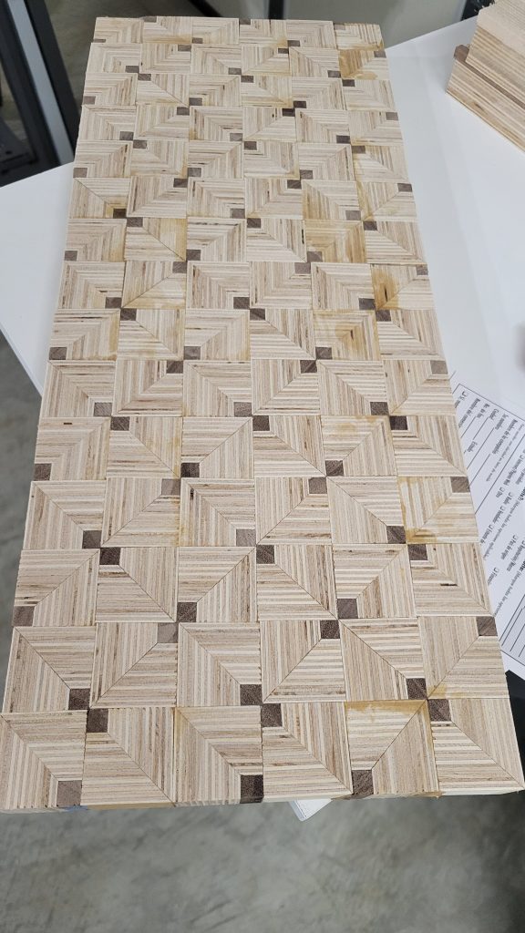 Close view of the patterned plywood and walnut strip layout before slicing into panel pieces.