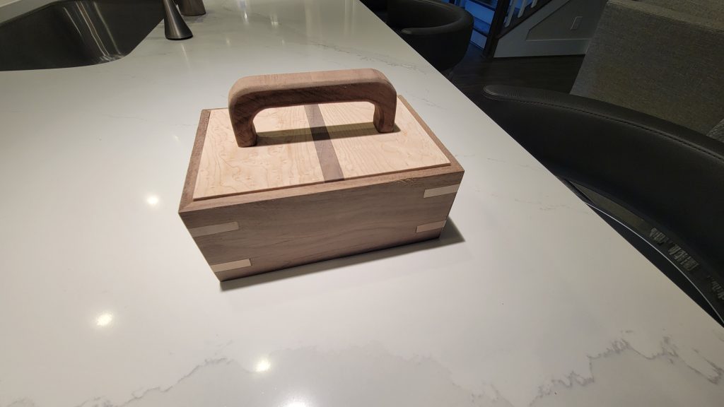 Rectangular wooden box with a handmade handle attached to the lid.