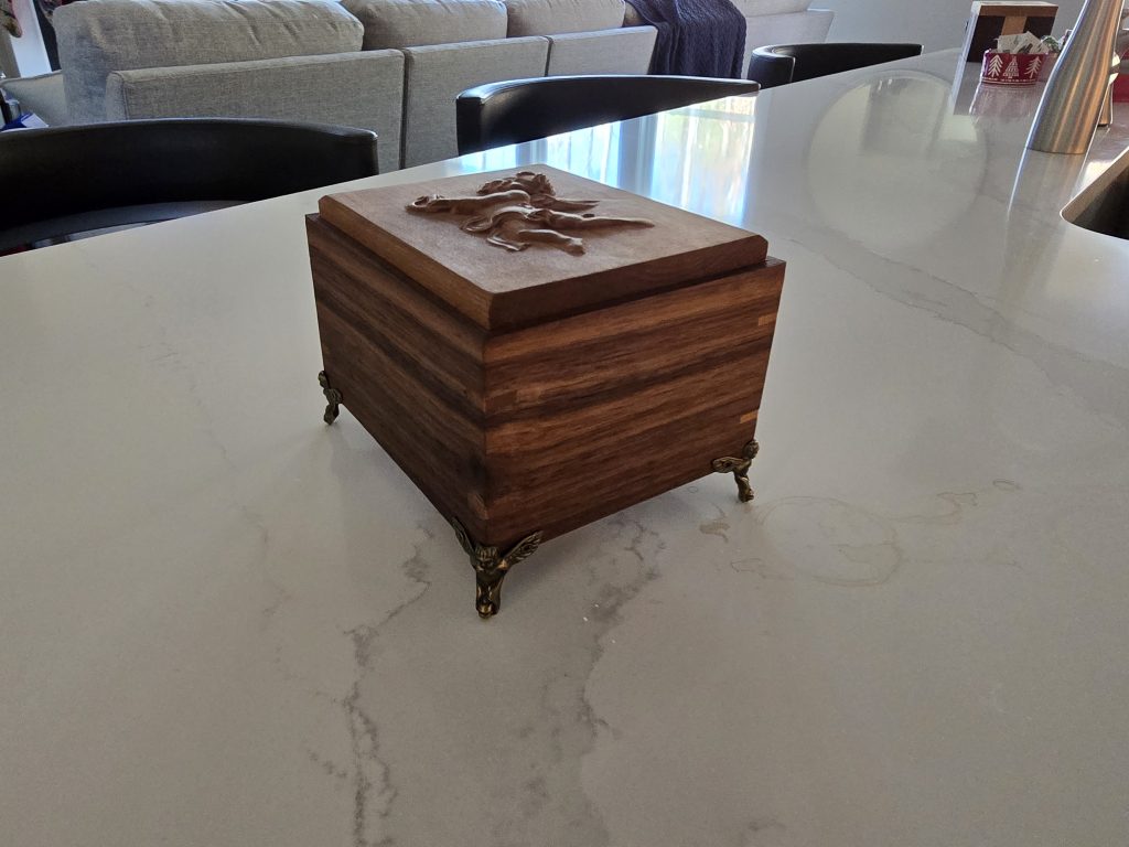 Side view of the finished walnut gift box showing the raised metal feet and cherry lid.