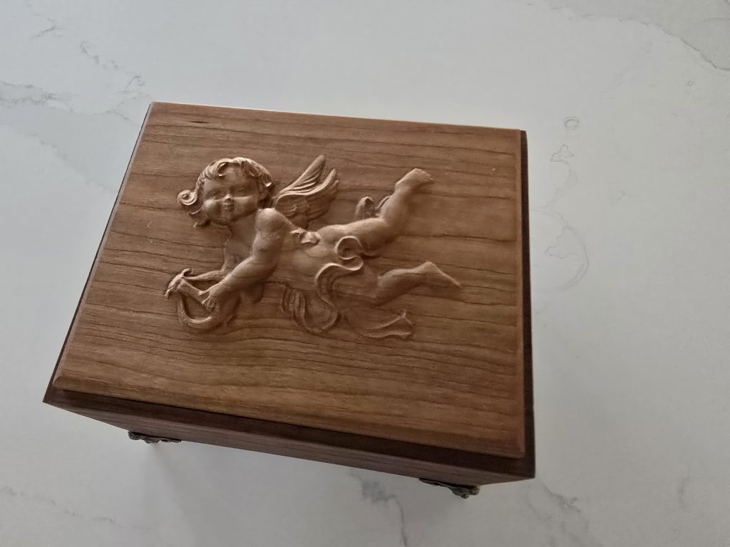 Close view of the cherry gift box lid with a raised CNC-carved cherub angel relief.