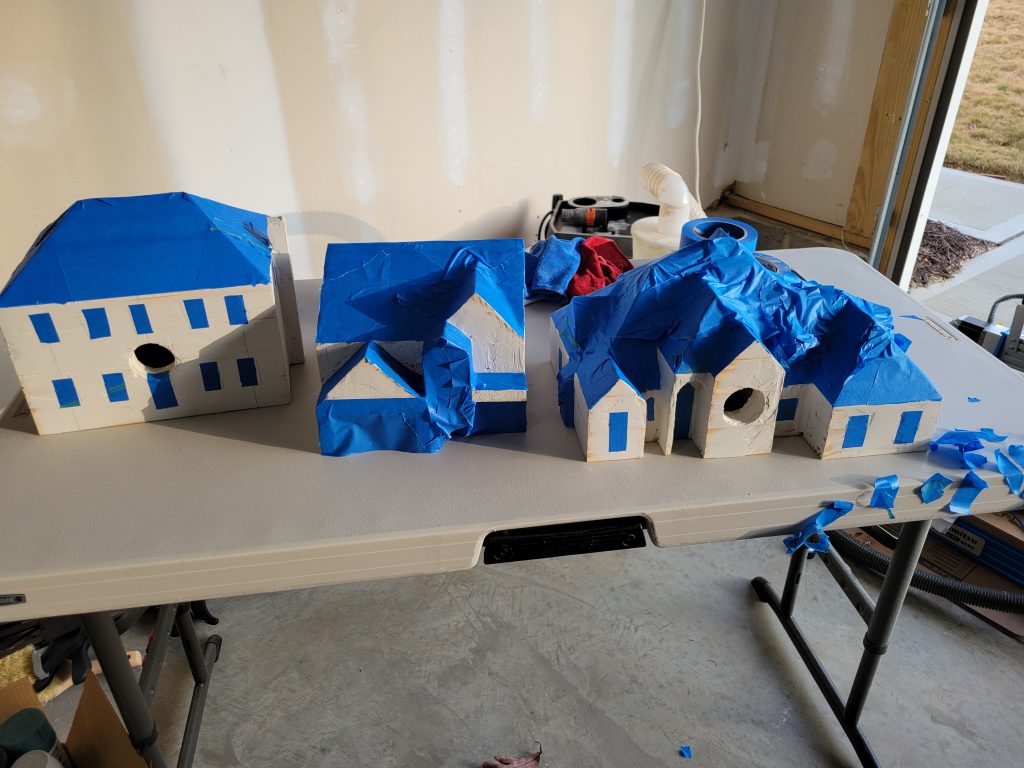 Birdhouse masked with blue tape during the textured brick spray paint stage