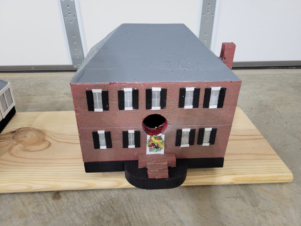 Finished brick-style custom birdhouse with gray roof, black shutters, front steps, chimney, and wreath