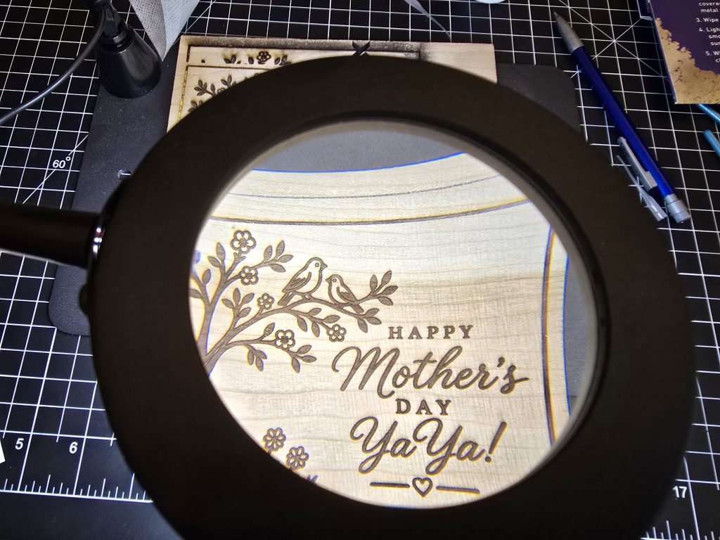 Close magnifier view of the engraved Mother's Day card details around the birds and lettering.
