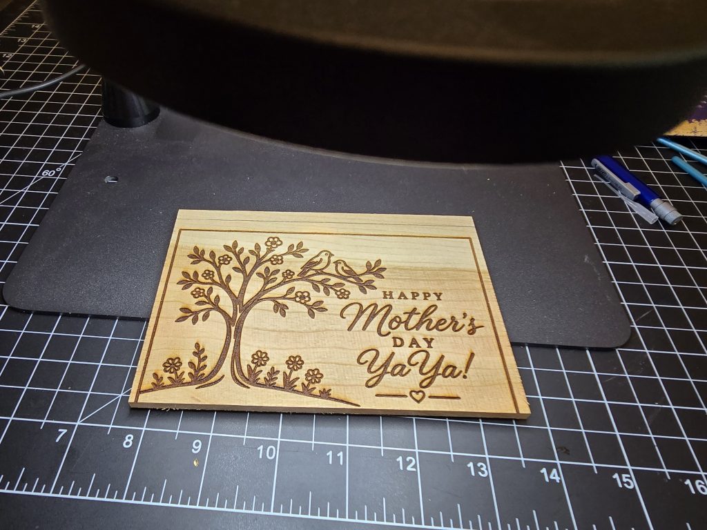 Engraved cherry wood Mother's Day card blank on a cutting mat before the white paint and foil finish.
