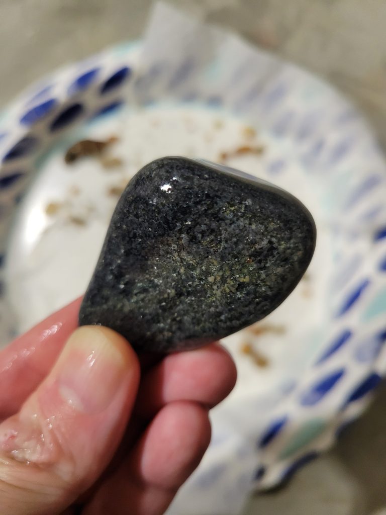 A dark polished rock held in hand after tumbling.
