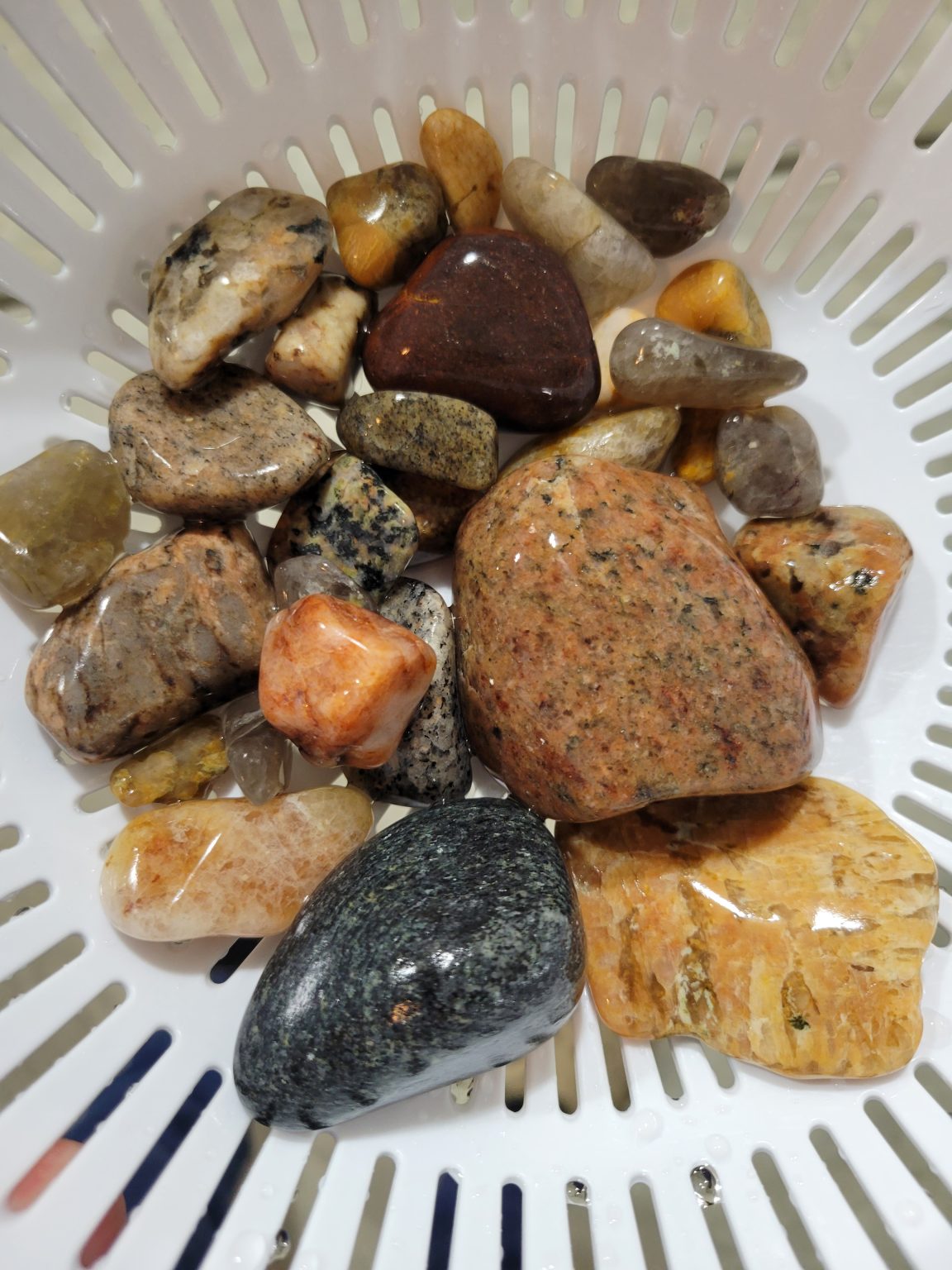 Glossy polished yard rocks in a white colander after tumbling.
