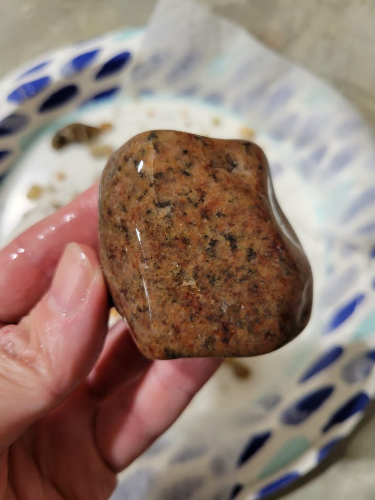 A reddish brown polished rock held in hand after tumbling.